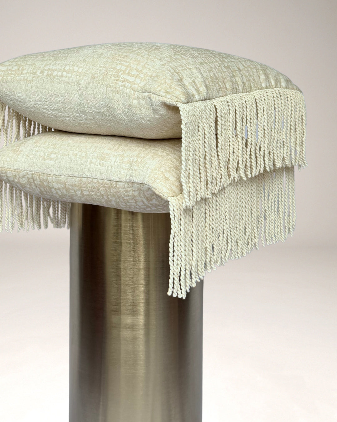 Crèmekleurig Hogaría sierkussen met fijne textuur en lange, gedraaide franjes aan de zijkanten, luxe handgemaakt interieurkussen in zacht neutraal design, perfect voor moderne en warme woonruimtes.