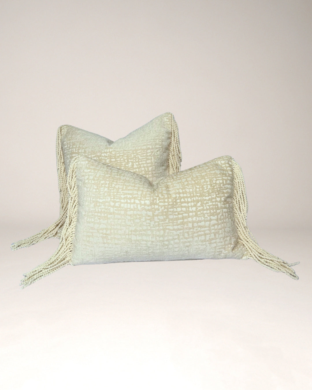 Crèmekleurig Hogaría sierkussen met fijne textuur en lange, gedraaide franjes aan de zijkanten, luxe handgemaakt interieurkussen in zacht neutraal design, perfect voor moderne en warme woonruimtes.